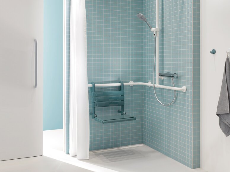Patiëntenbadkamer met HEWI serie 477 Doucheruimte van een patiëntenbadkamer in blauw en wit met uitzicht door een schuifdeur